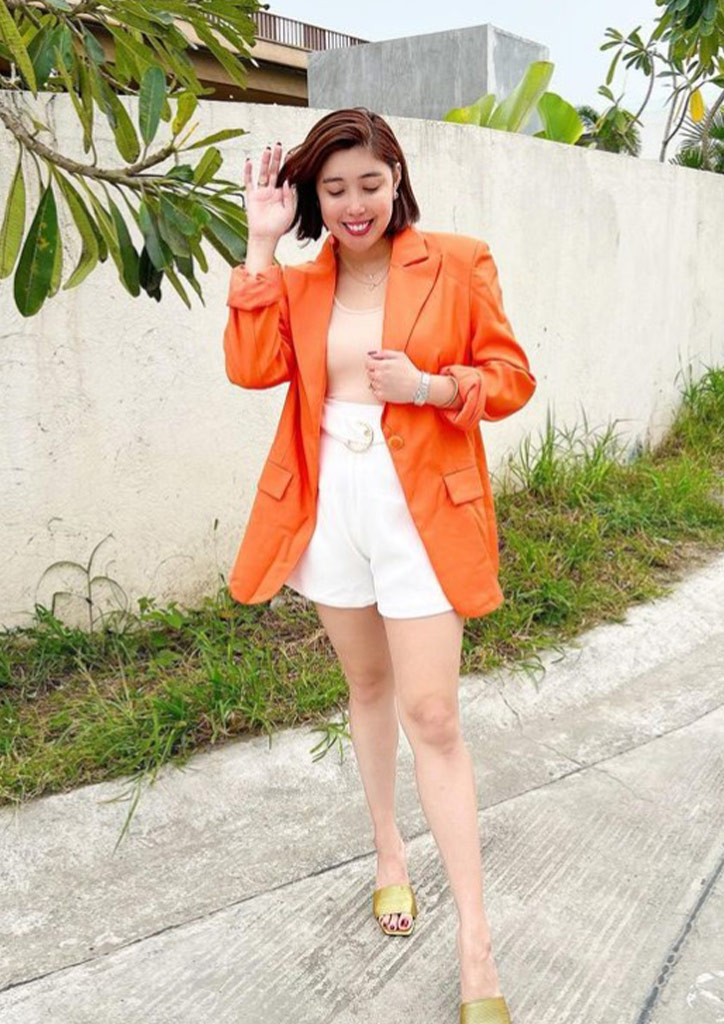  Dani Barretto makes her orange blazer pop with her neutrals and olive green slip-on sandals.