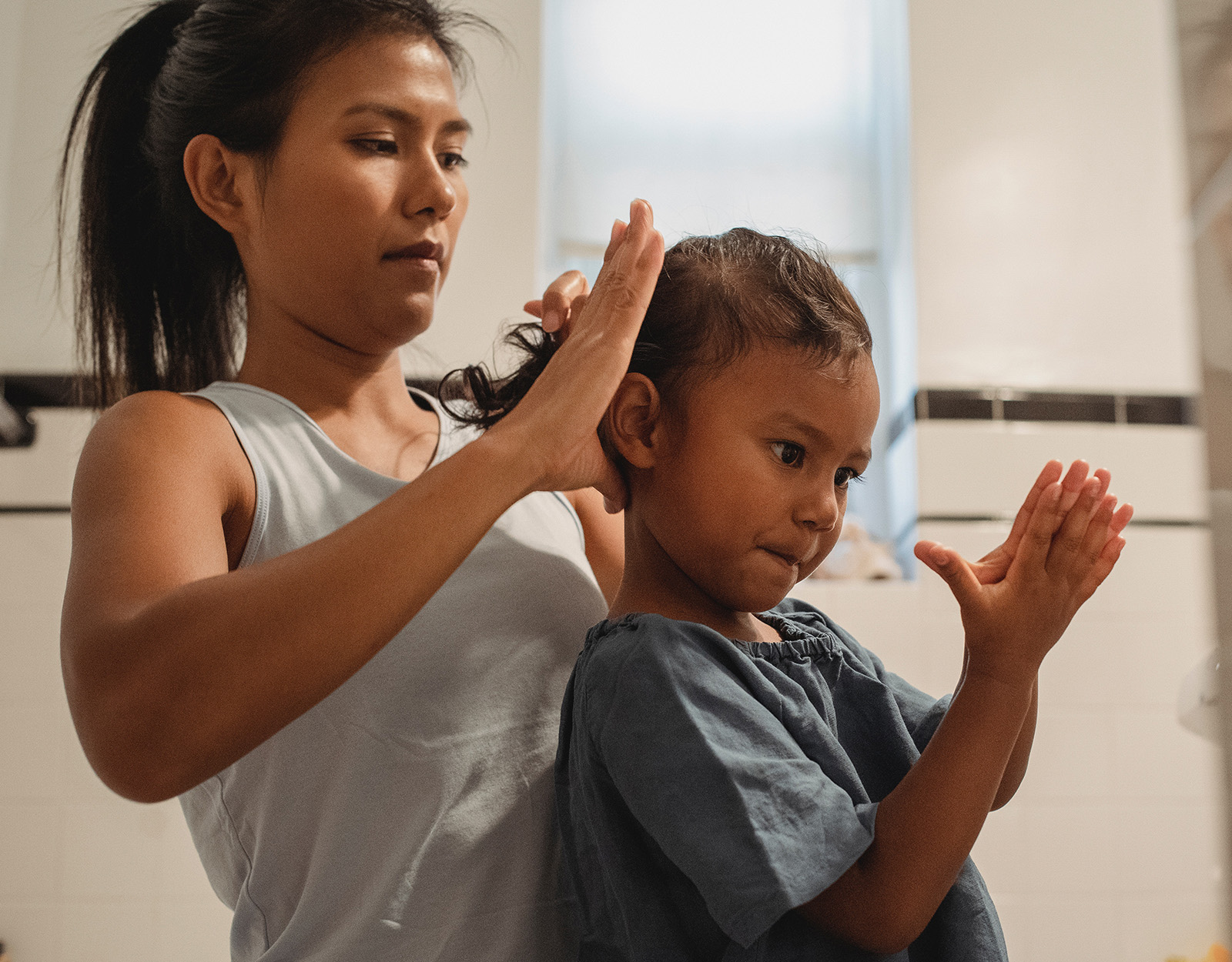 A millennial parent tying her daughter's hair
